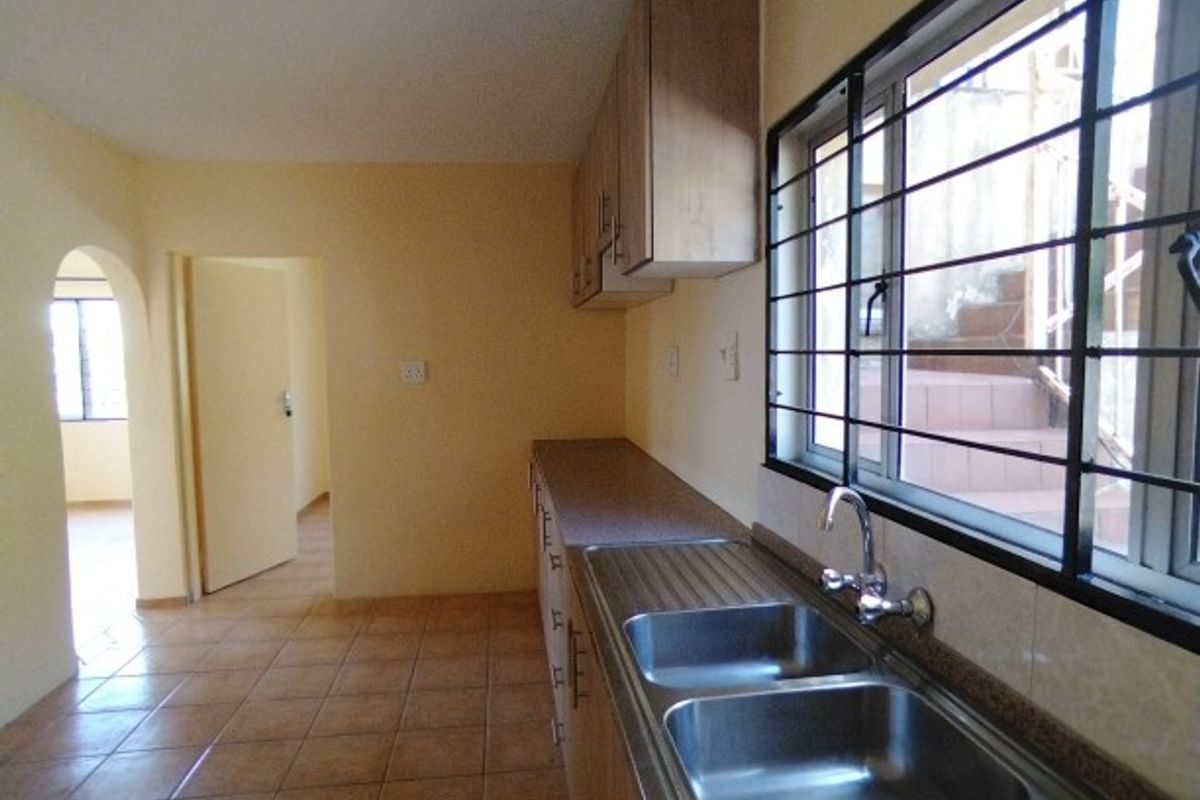 A functional kitchen featuring tiled flooring, built-in cabinetry, and a double stainless steel sink with a view through a window with security bars.
