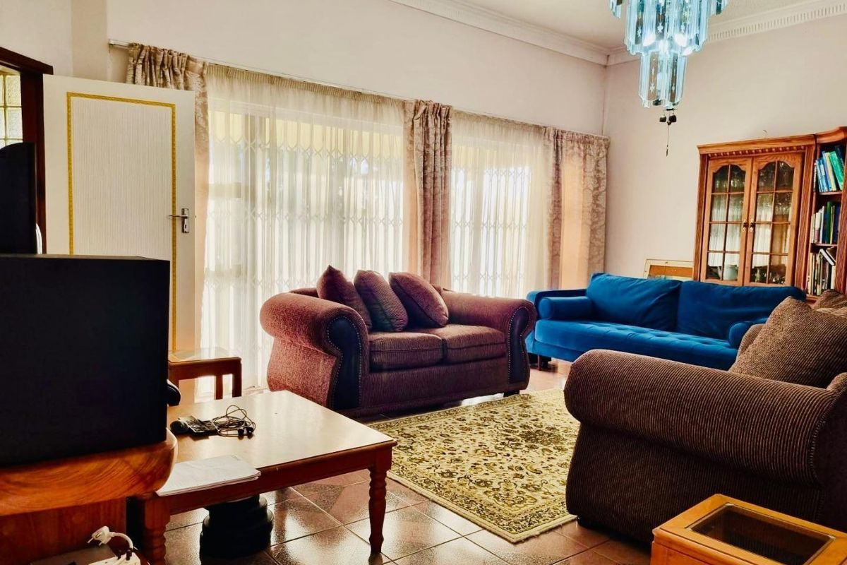 A spacious living room featuring tiled flooring, decorative ceiling cornices, and large sliding glass doors that provide access to the exterior.