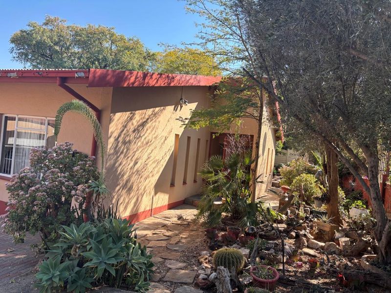 A view of the rear exterior of the house featuring a stone pathway, established garden landscaping, and a metal roof structure.