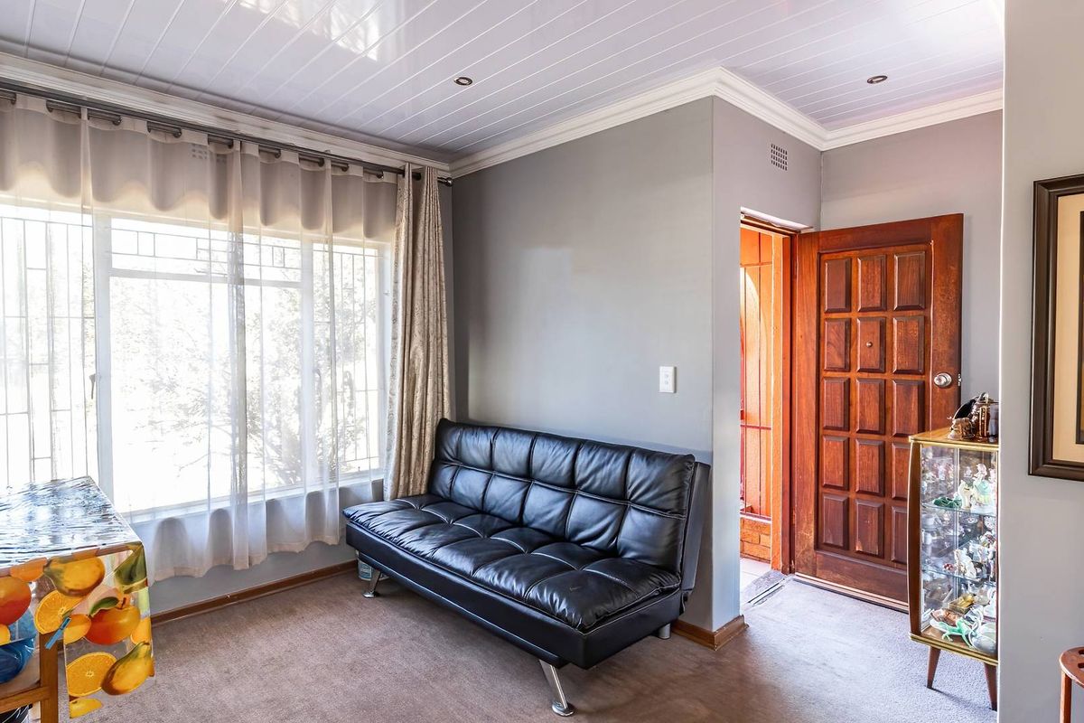 A living room featuring carpet flooring, a large window with security bars, and a solid timber entrance door.