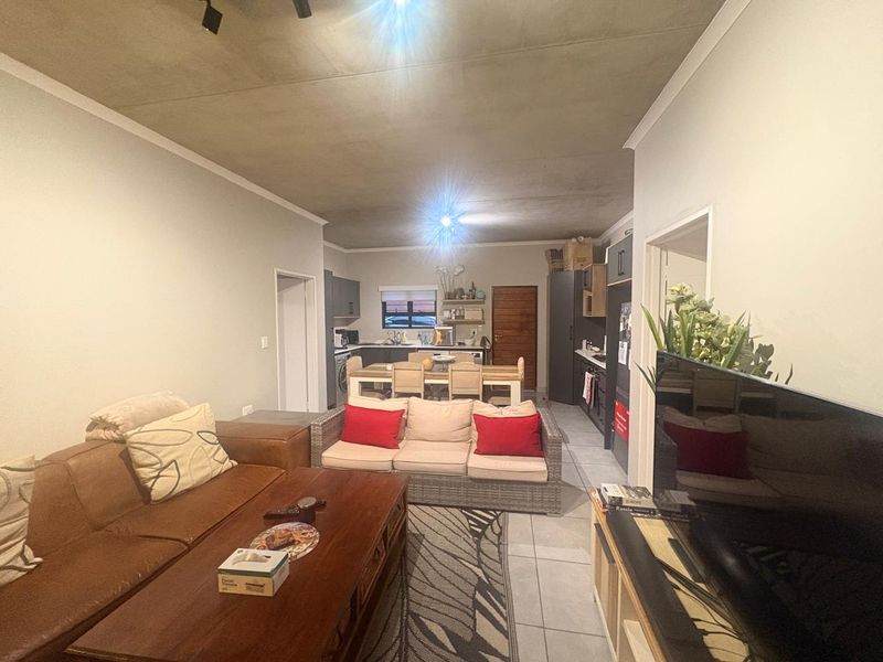 Open-plan living and kitchen area featuring tiled floors, modern cabinetry, and an exposed concrete ceiling, creating a functional and connected living space.