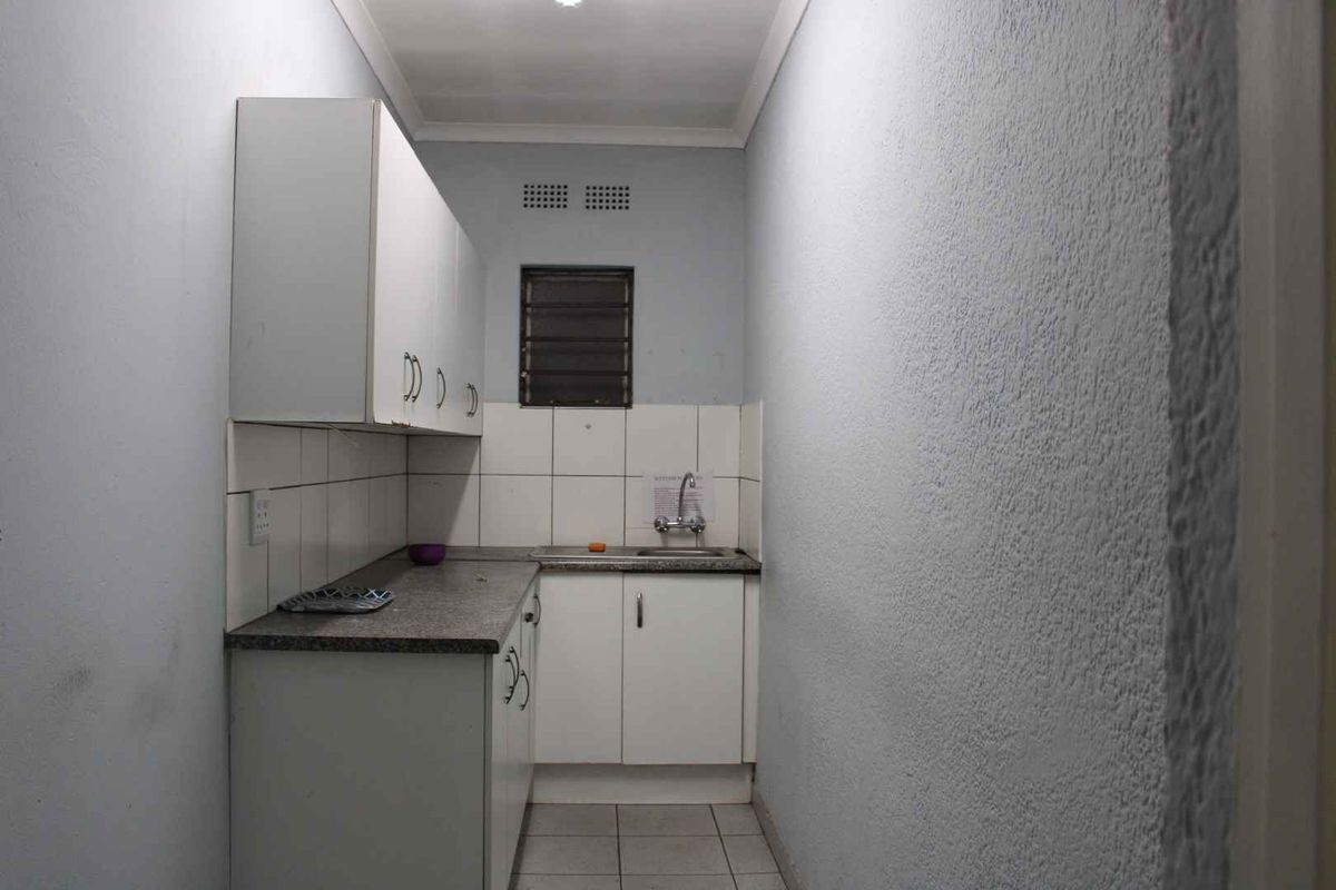 A compact, functional kitchen area featuring built-in cabinetry, a stainless steel sink, and tiled splashbacks, offering a practical space for food preparation.