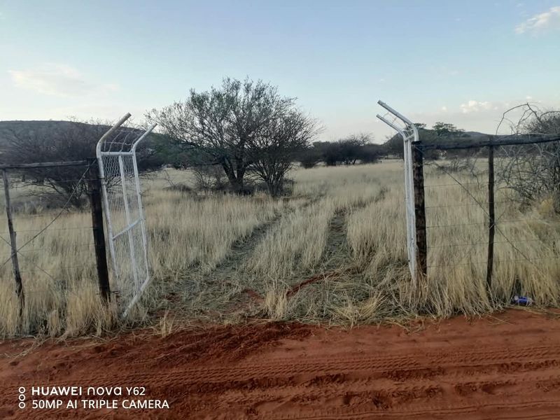 A view of the property entrance featuring a metal gate and wire fencing leading into an open agricultural field.