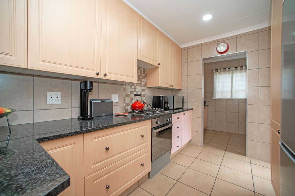 A functional kitchen featuring light wood cabinetry, granite countertops, a gas hob, and an integrated oven, with a tiled backsplash and floor.