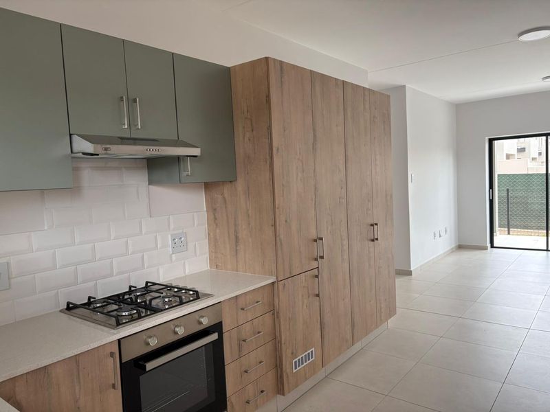 Modern open-plan kitchen featuring wood-look cabinetry, stone countertops, gas hob, and subway tile backsplash, flowing into a bright living area with patio access.