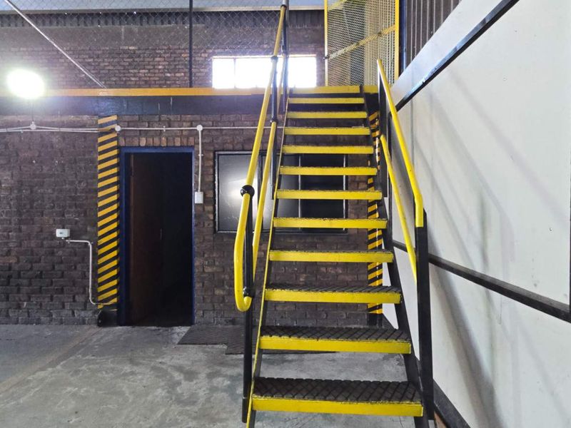 Industrial utility space featuring a metal staircase leading to a mezzanine level with exposed brick walls and functional safety railings.