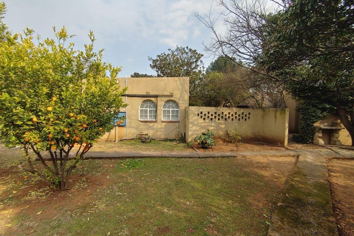 Rear exterior view of the property featuring a garden area, arched windows, and a decorative breeze block wall with paved pathways.