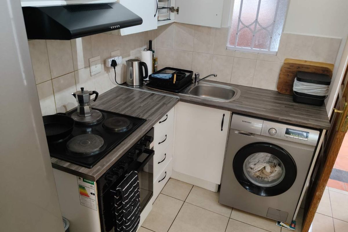 Compact kitchen featuring laminate countertops, electric hob, built-in oven, extractor fan, stainless steel sink, and tiled finishes with integrated laundry appliance space.