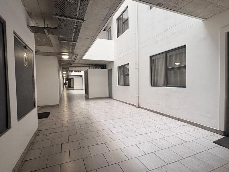 A clean, industrial-style apartment hallway featuring tiled flooring, exposed concrete ceilings with cable management, and multiple unit access points.