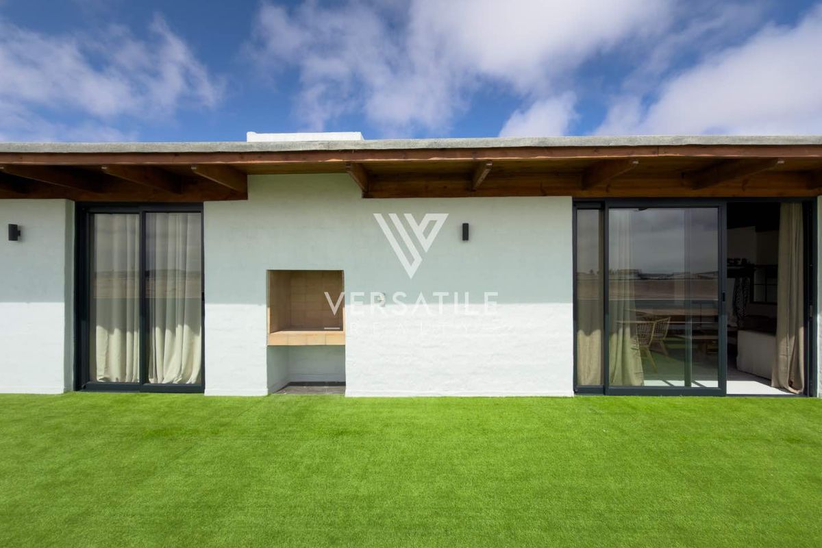 Rear exterior view of the townhouse featuring a covered patio area with a built-in braai, sliding glass doors, and artificial lawn.