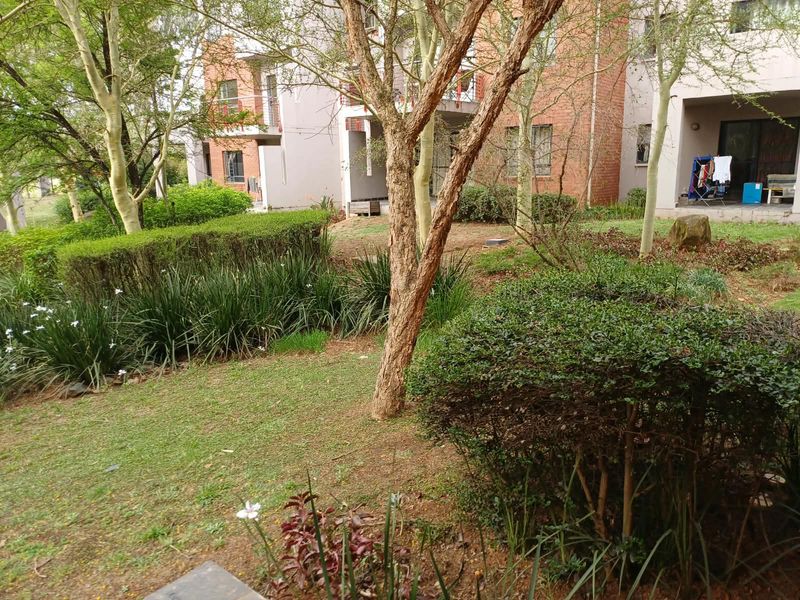 A view of the rear exterior of the apartment building, featuring a landscaped garden area and access to ground-floor patios.
