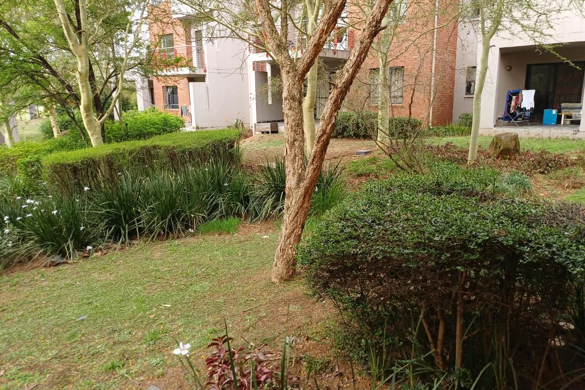 A view of the rear exterior of the apartment building, featuring a landscaped garden area and access to ground-floor patios.