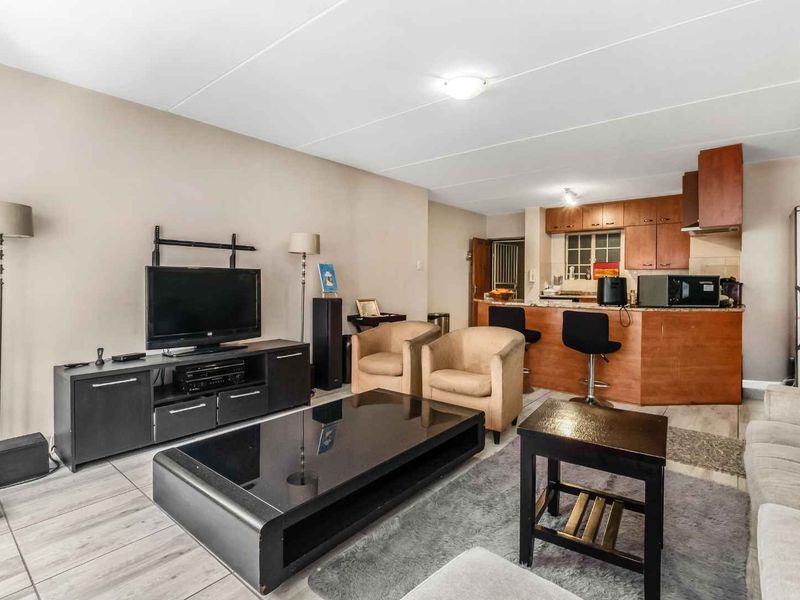 Open-plan living area featuring a kitchen with breakfast bar and cabinetry, seamlessly flowing into a comfortable lounge space with tiled flooring throughout.