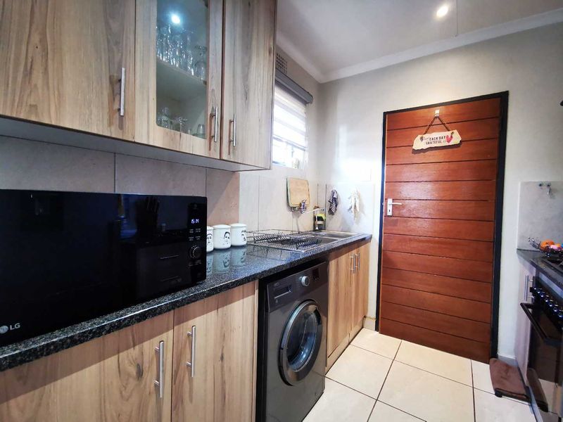 A functional scullery featuring wood-look cabinetry, granite countertops, a stainless steel sink, and tiled flooring, providing additional prep and laundry space.