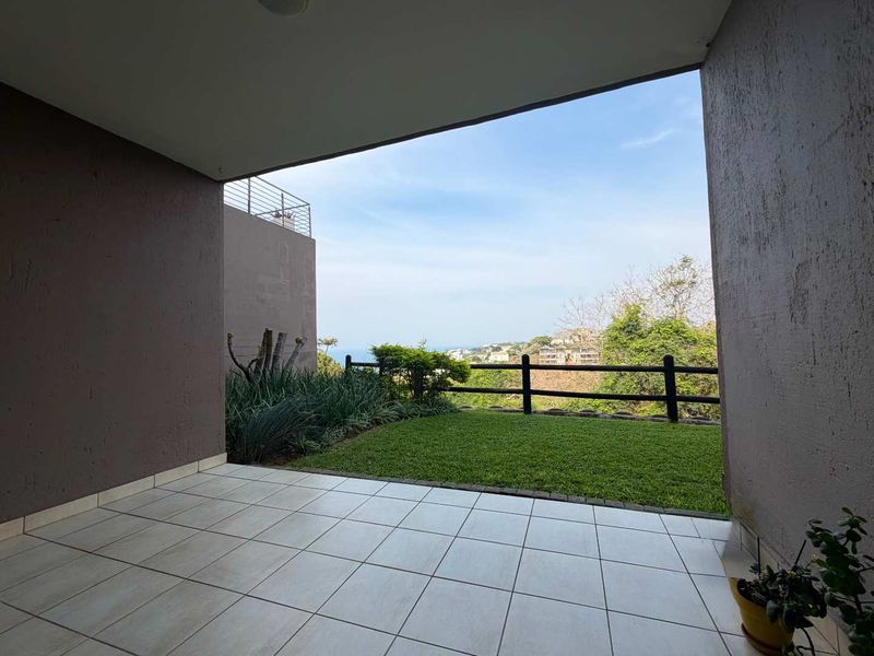 A covered patio featuring tiled flooring, overlooking a private garden area with a timber fence and scenic coastal views.