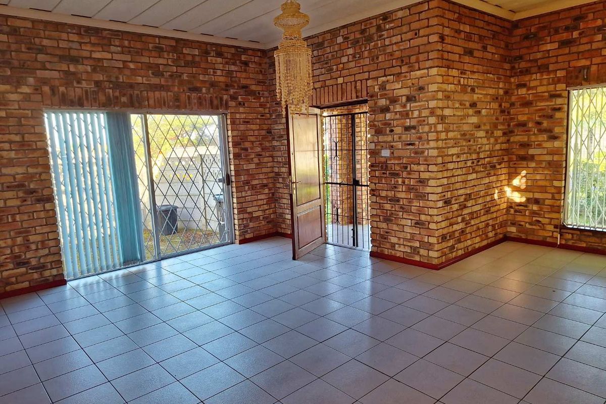 Spacious living area featuring exposed face-brick walls, tiled flooring, and sliding glass doors with security gates leading to the exterior.