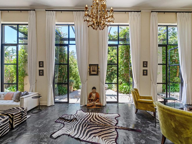 Elegant living room featuring high ceilings, large black-framed glass doors opening to a lush garden, and polished concrete flooring.