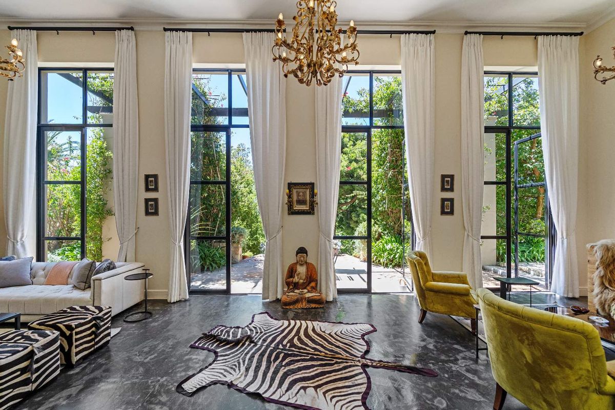 Elegant living room featuring high ceilings, large black-framed glass doors opening to a lush garden, and polished concrete flooring.