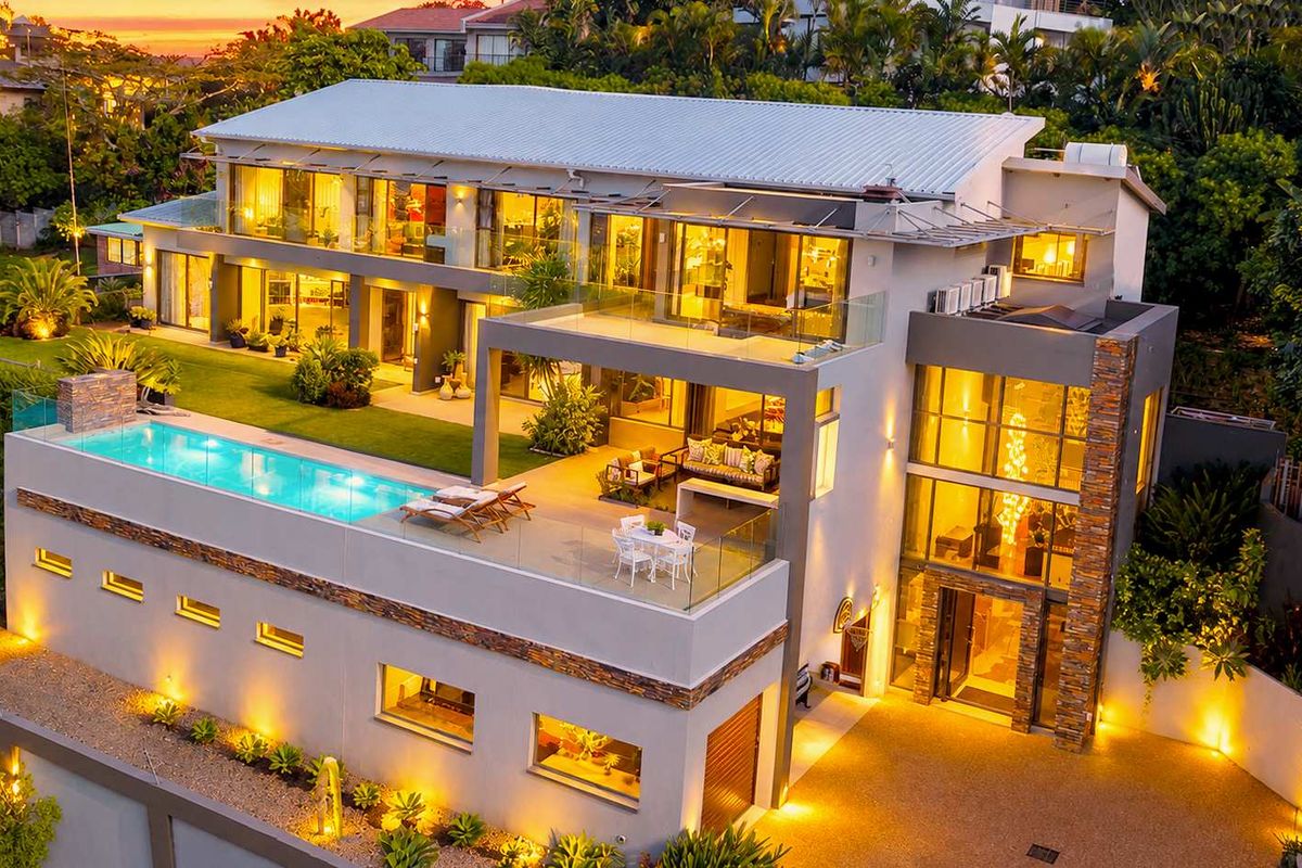 Stunning aerial view of a modern multi-level luxury residence featuring a swimming pool, expansive terraces, stone accents, and beautifully landscaped grounds.