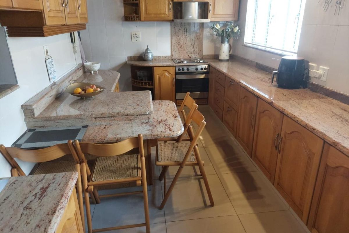 A functional kitchen featuring wooden cabinetry, granite countertops, a built-in oven, and a gas hob with an integrated extractor fan.