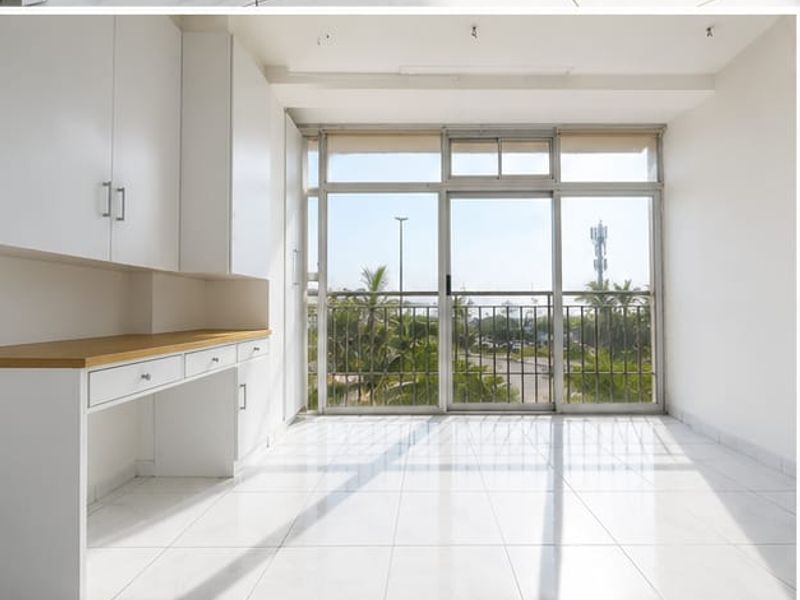 Bright and empty office space featuring built-in desk and cabinetry, tiled flooring, and large sliding glass doors leading to a balcony.