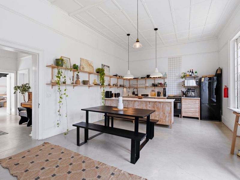 Spacious open-plan kitchen and dining area featuring a central island, open shelving, pendant lighting, and polished concrete floors under a classic coffered ceiling.