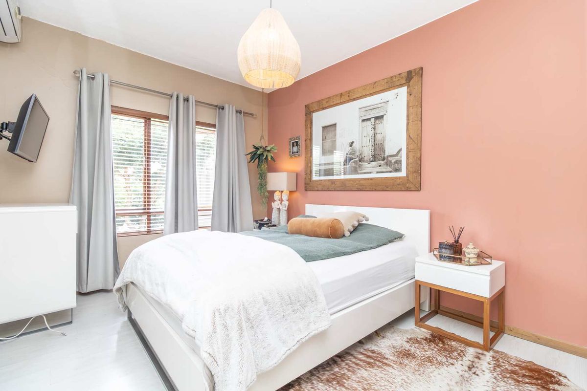A well-lit bedroom featuring a feature wall, wooden window blinds, and a wall-mounted air conditioning unit.