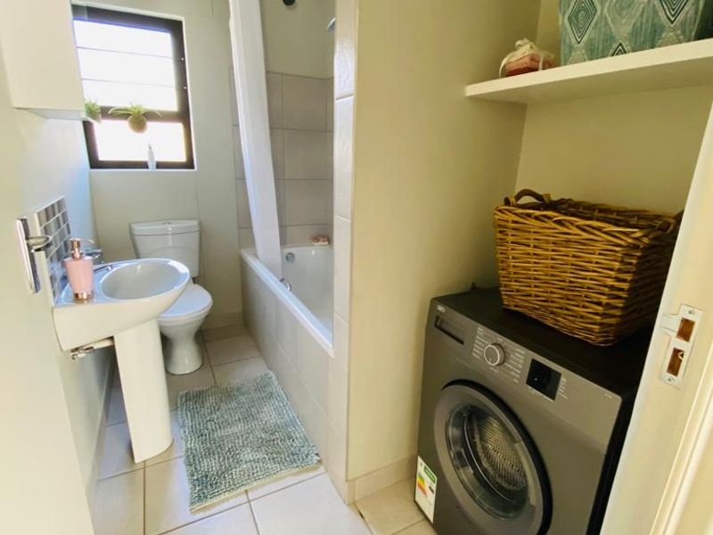 A functional bathroom featuring a pedestal basin, toilet, and bathtub with shower, complemented by integrated laundry space and built-in shelving.