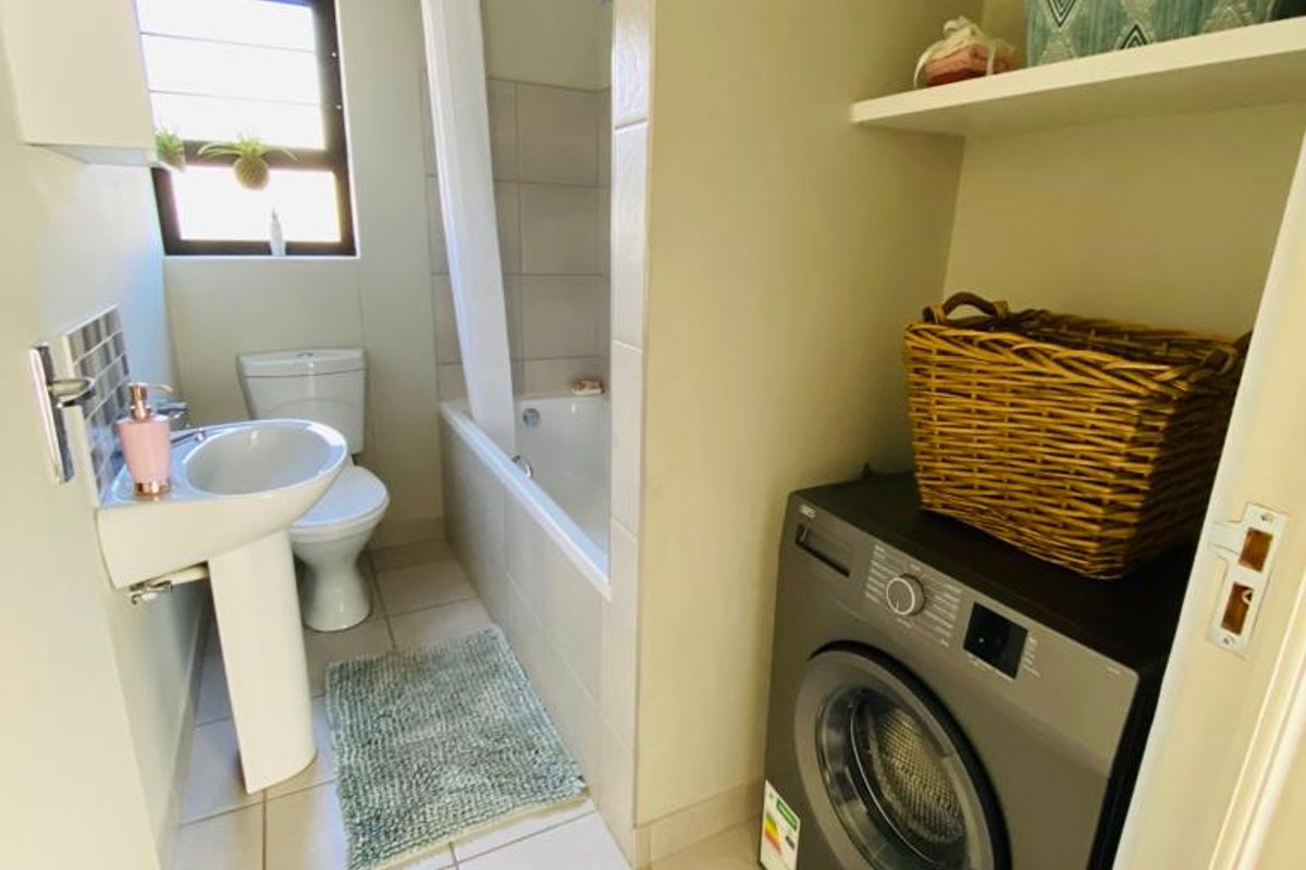 A functional bathroom featuring a pedestal basin, toilet, and bathtub with shower, complemented by integrated laundry space and built-in shelving.