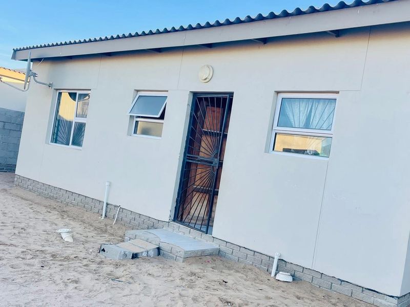 Rear exterior view of the house featuring a security gate, aluminium windows, and unfinished ground area requiring landscaping.