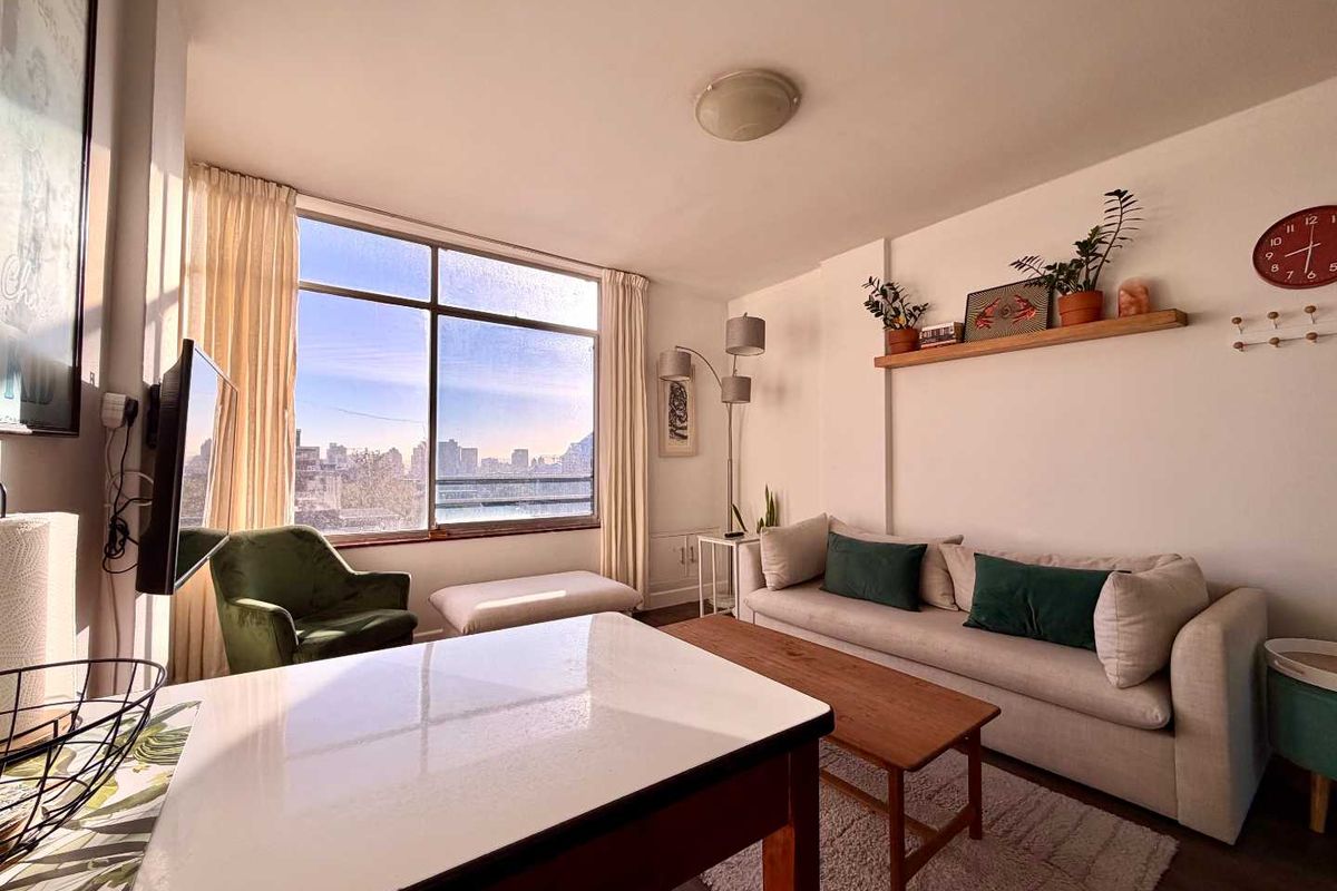 A bright living room featuring a large window with city views, neutral walls, and wood-look flooring.