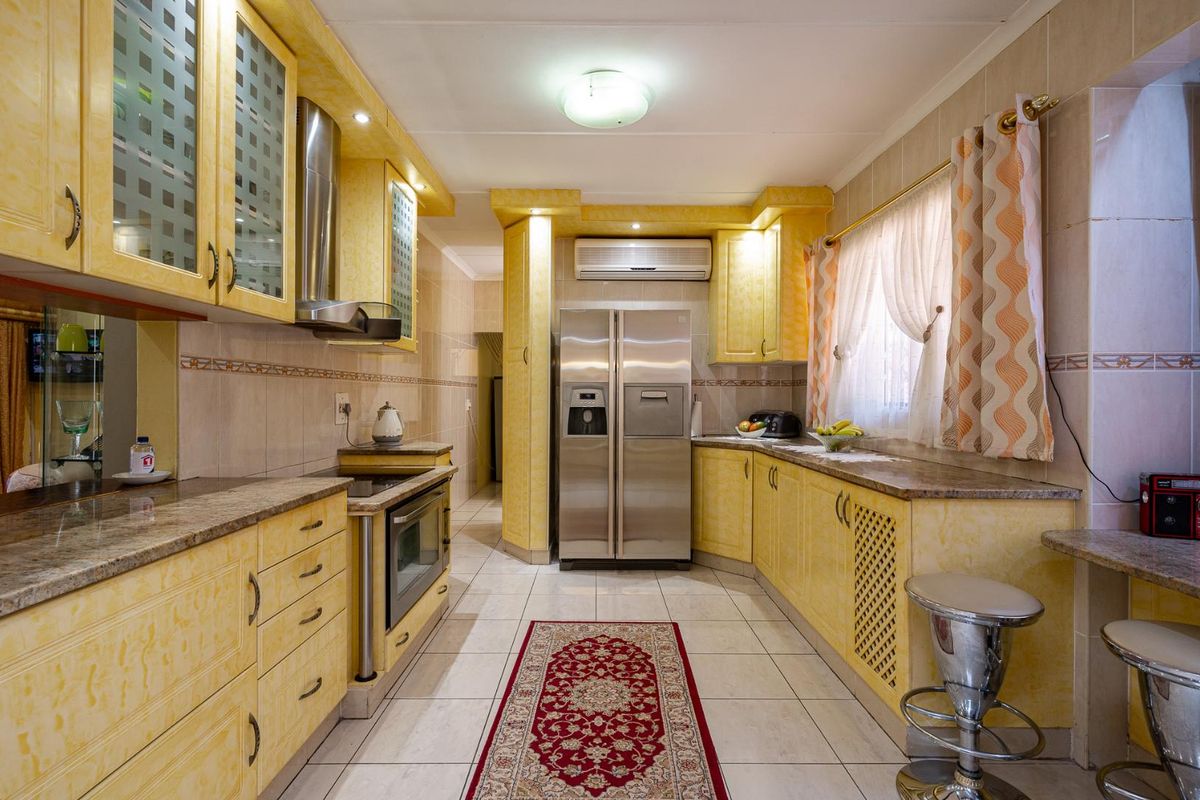 A functional kitchen featuring yellow cabinetry, granite countertops, a built-in oven, stainless steel extractor fan, and a wall-mounted air conditioning unit.