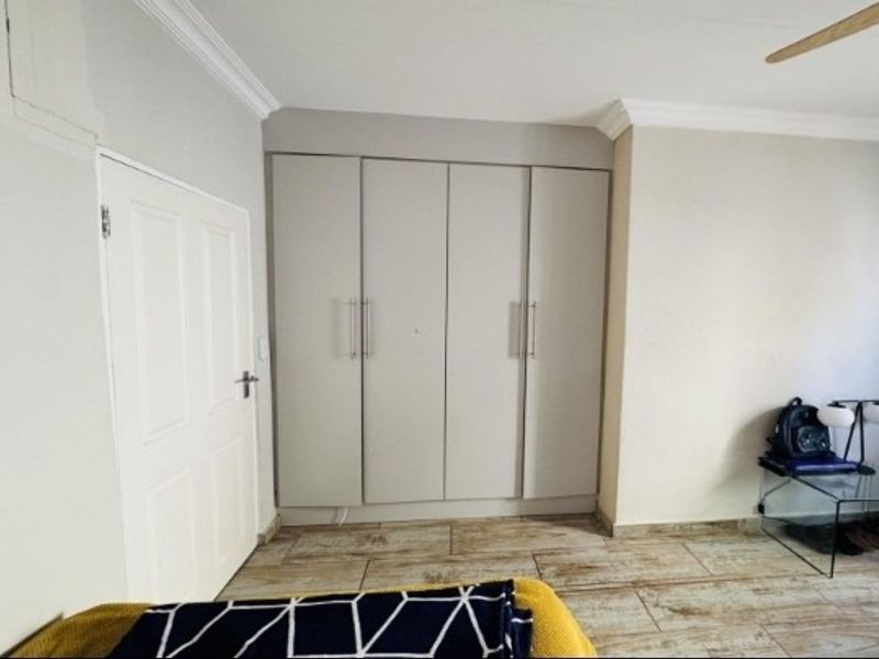 A bedroom featuring built-in cupboards, tiled flooring, and a ceiling fan, offering a clean and functional living space.