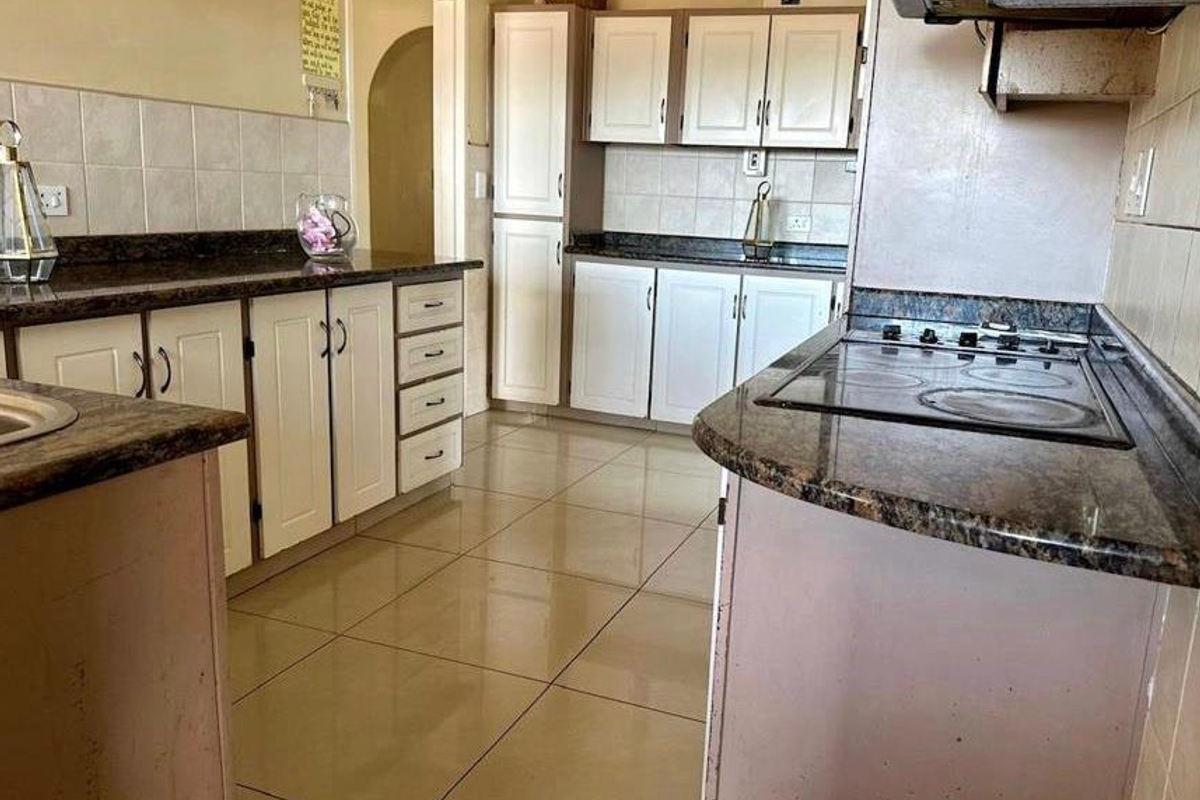 A functional kitchen featuring granite countertops, tiled flooring, and built-in cabinetry with an integrated electric hob and extractor fan.