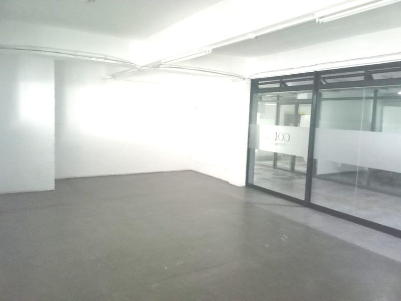 An empty, open-plan office space featuring concrete flooring, exposed ceiling conduit, and a modern glass partition wall.