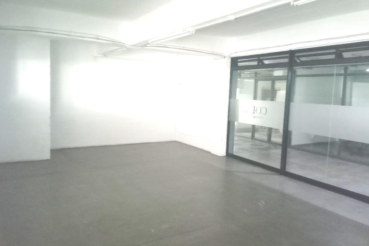 An empty, open-plan office space featuring concrete flooring, exposed ceiling conduit, and a modern glass partition wall.