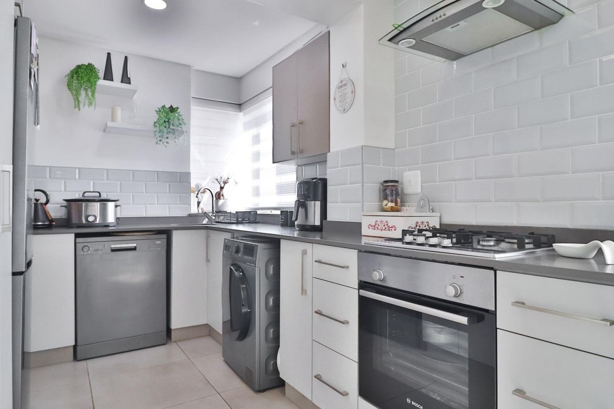 Modern kitchen featuring white cabinetry, subway tile backsplash, stone countertops, built-in oven, gas hob, and stainless steel extractor fan.
