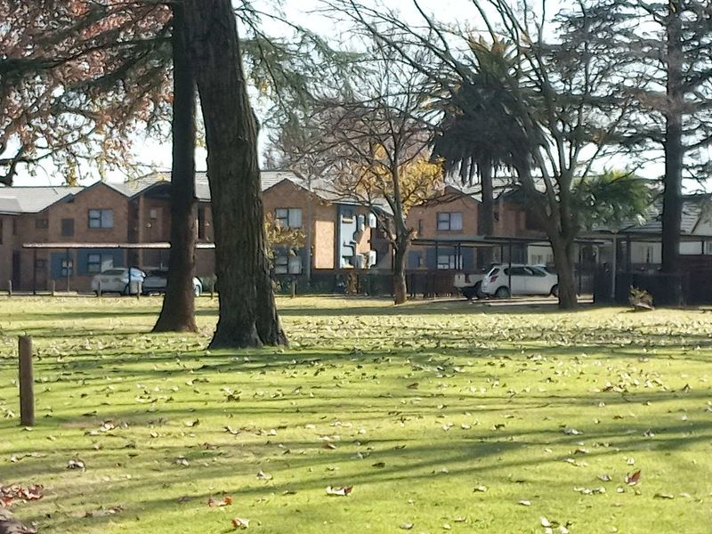 A view of the townhouse complex exterior, featuring brick facades, tiled roofing, and established trees within a communal garden setting.