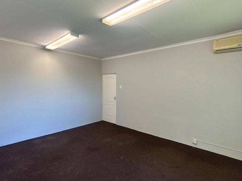 A clean, empty office space featuring neutral walls, dark carpeting, fluorescent lighting, and a wall-mounted air conditioning unit.
