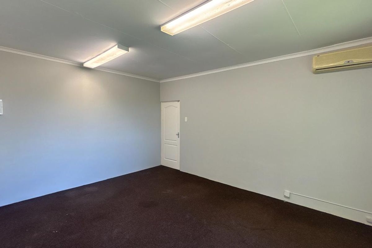 A clean, empty office space featuring neutral walls, dark carpeting, fluorescent lighting, and a wall-mounted air conditioning unit.