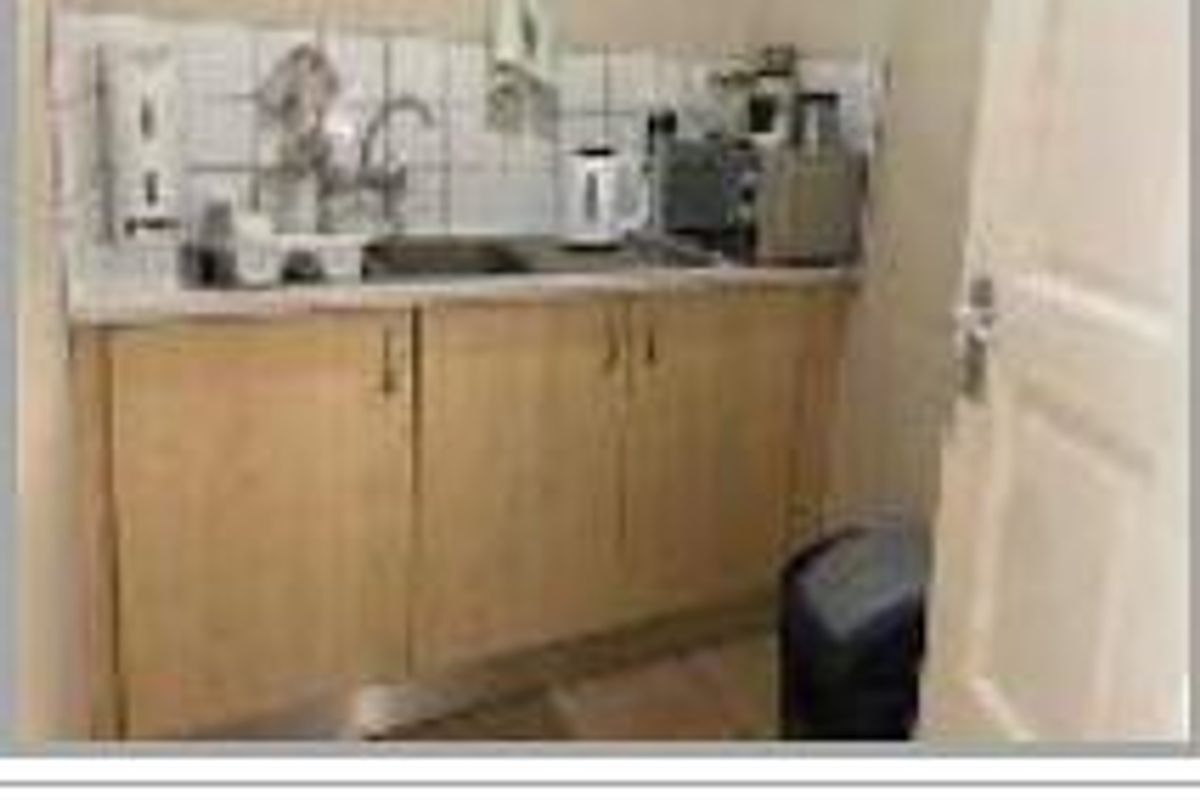 A compact office kitchenette featuring basic cabinetry, a stainless steel sink, and a tiled backsplash.
