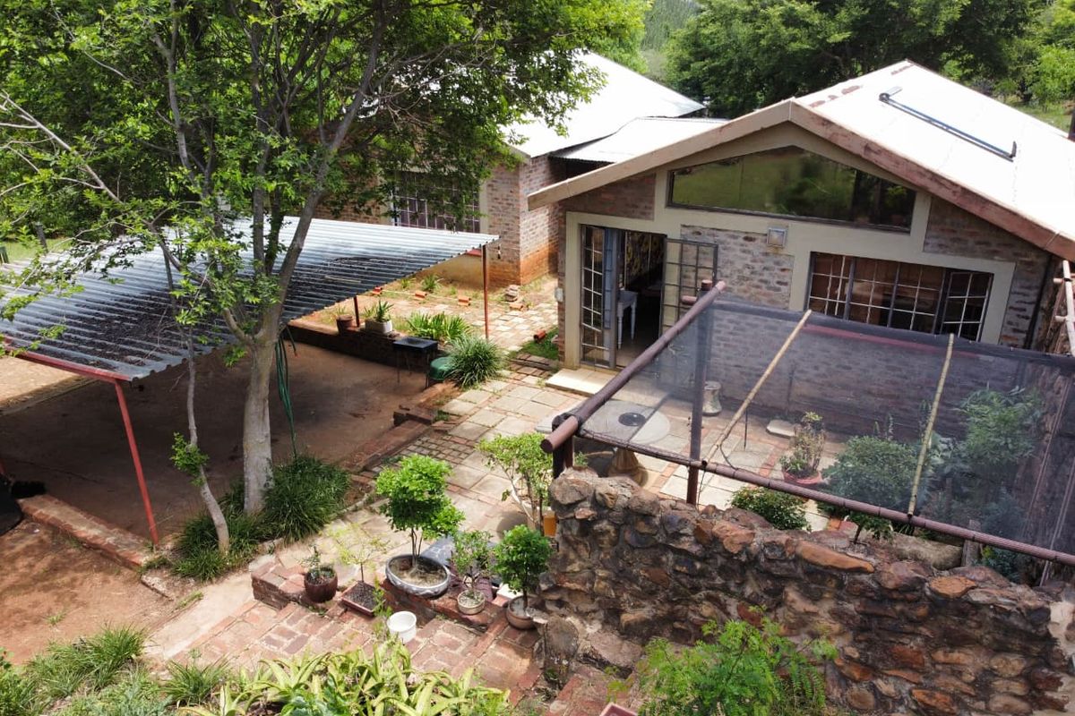 An elevated view of the rear exterior featuring a brick dwelling with a corrugated roof, a covered carport, and a stone-walled patio area.