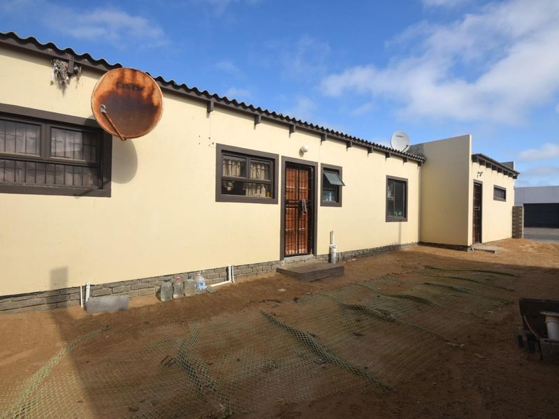 Rear exterior view of the property featuring a sandy yard, security gates, and basic building finishes.
