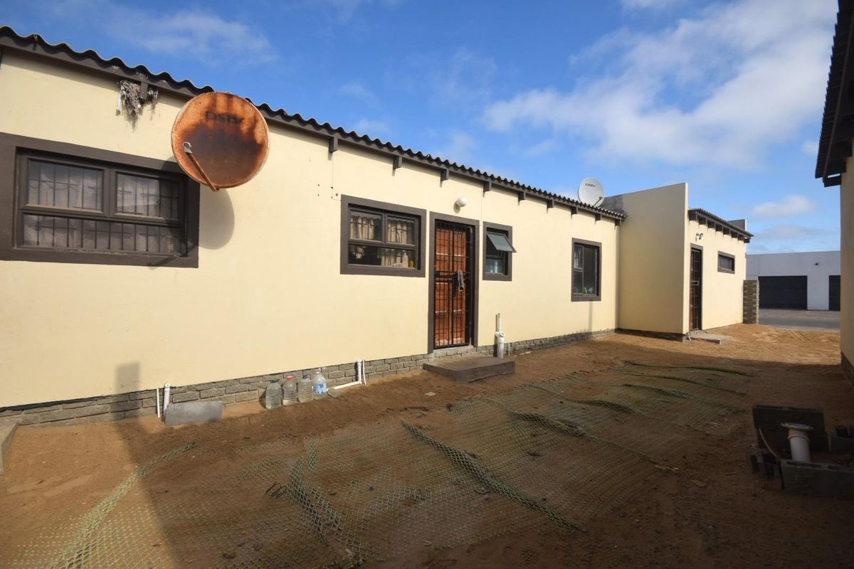 Rear exterior view of the property featuring a sandy yard, security gates, and basic building finishes.
