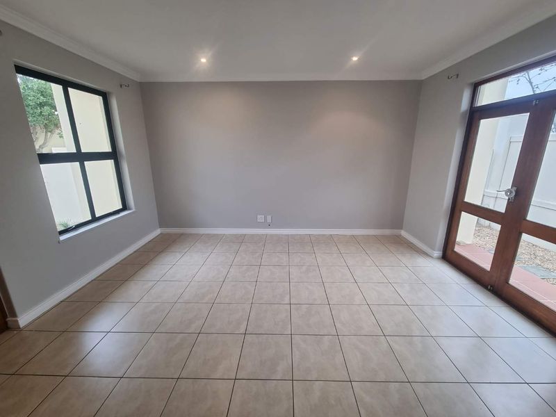 A bright and spacious living area featuring neutral tiled flooring, recessed downlighting, and direct access to the exterior through a timber framed glass door.