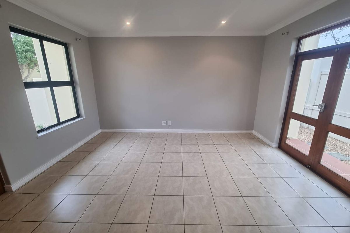 A bright and spacious living area featuring neutral tiled flooring, recessed downlighting, and direct access to the exterior through a timber framed glass door.