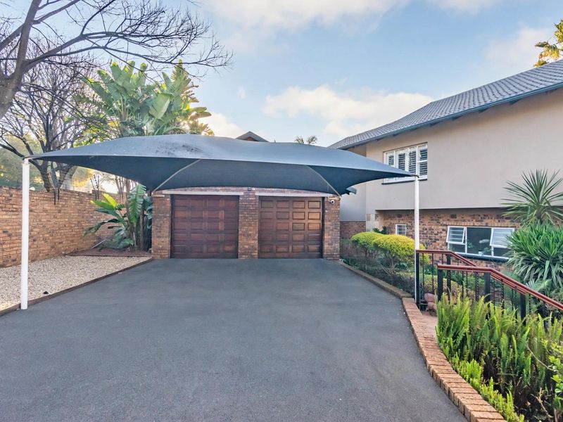 Front exterior view featuring a double garage with wooden doors, a shade sail carport, and a paved driveway with established garden borders.