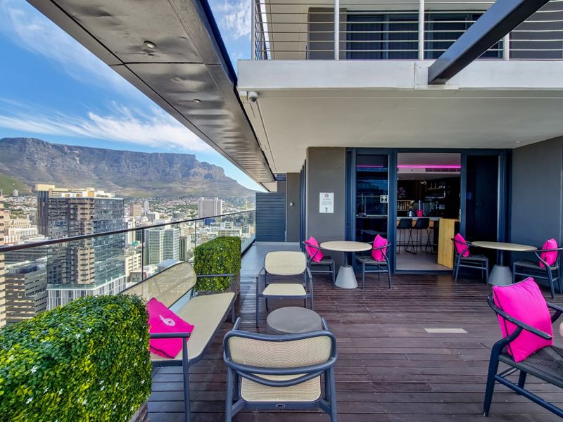 Spacious covered balcony featuring timber decking, glass balustrades, and panoramic city and mountain views, providing an ideal outdoor entertainment space.