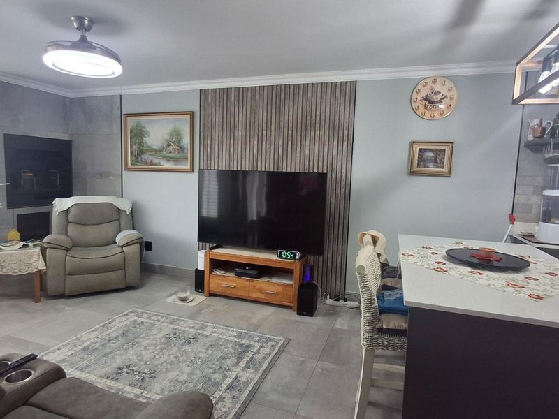Spacious open-plan living area featuring a modern kitchen island, stone-look fireplace surround, and a decorative slatted wood feature wall with tiled flooring throughout.