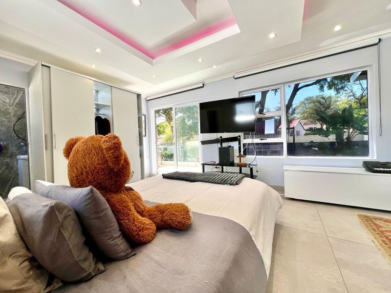 A modern bedroom featuring built-in wardrobes, recessed ceiling lighting with ambient accents, and large sliding glass doors providing ample natural light.